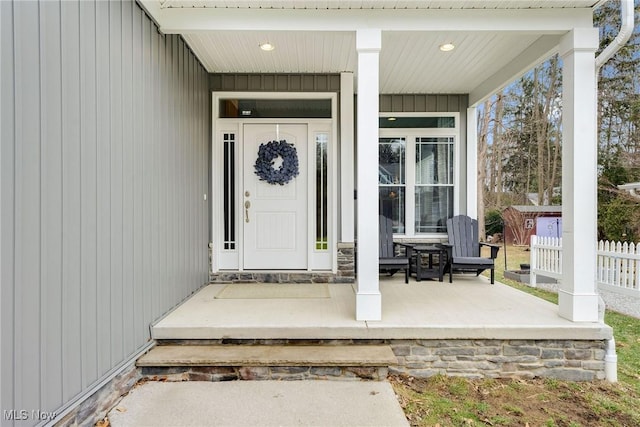 view of exterior entry featuring fence and a porch