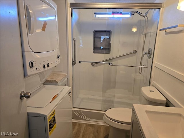 full bath with toilet, stacked washer / dryer, wood finished floors, vanity, and a stall shower