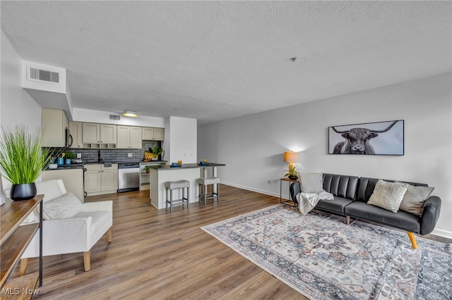 living area with light wood-style floors, visible vents, a textured ceiling, and baseboards