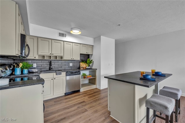 kitchen with a breakfast bar, dark countertops, visible vents, a sink, and black appliances