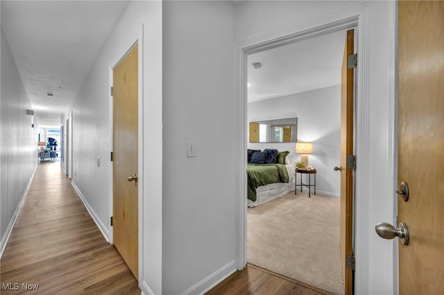 corridor with carpet floors, wood finished floors, and baseboards