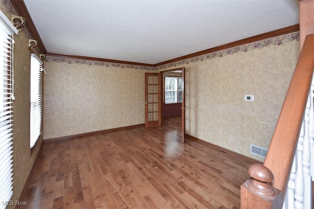 empty room with french doors, crown molding, visible vents, wood finished floors, and baseboards