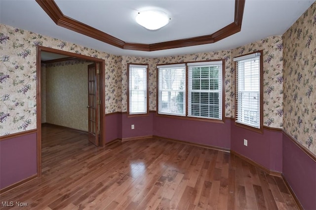 unfurnished room featuring a tray ceiling, wood finished floors, wainscoting, and wallpapered walls