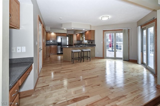 kitchen with stainless steel fridge, dark countertops, light wood-style flooring, a peninsula, and a kitchen bar