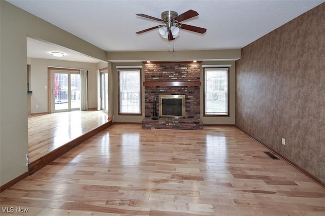 unfurnished living room with visible vents, light wood-style floors, a brick fireplace, ceiling fan, and baseboards