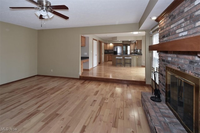 unfurnished living room featuring light wood finished floors, ceiling fan, a fireplace, and baseboards