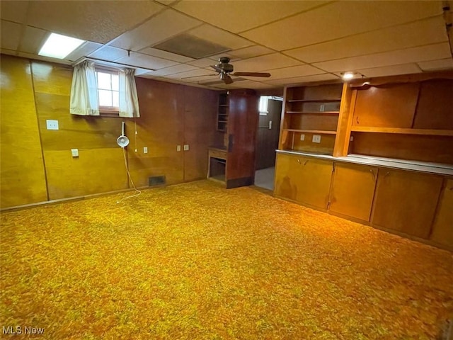 basement featuring visible vents, wood walls, a drop ceiling, and a ceiling fan