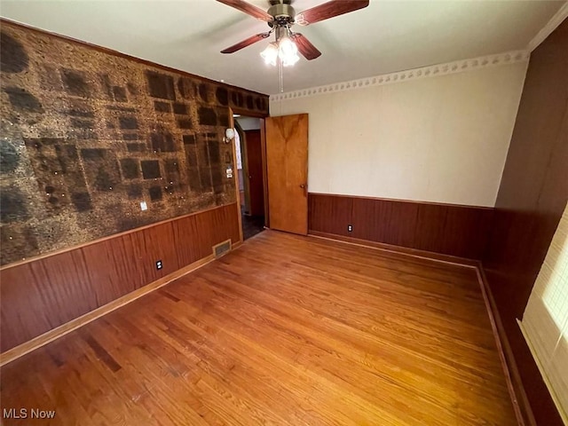 empty room with visible vents, a wainscoted wall, ceiling fan, wood finished floors, and wood walls