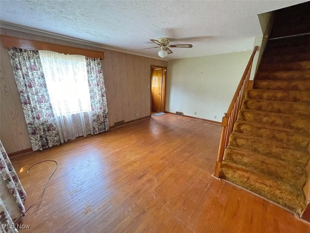 unfurnished living room with a ceiling fan, a textured ceiling, wood finished floors, baseboards, and stairs