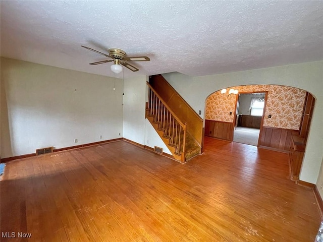 empty room with arched walkways, a wainscoted wall, visible vents, hardwood / wood-style floors, and stairs