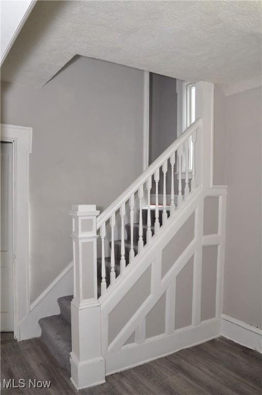 stairs with a textured ceiling, wood finished floors, and baseboards