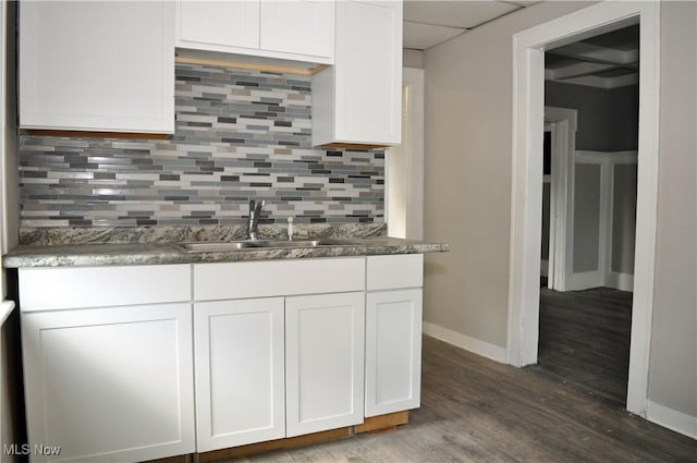 kitchen featuring wood finished floors, a sink, white cabinetry, baseboards, and backsplash