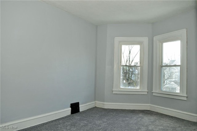 spare room featuring dark colored carpet and baseboards