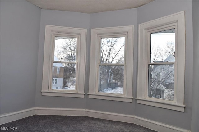 interior space with dark colored carpet, a wealth of natural light, and baseboards