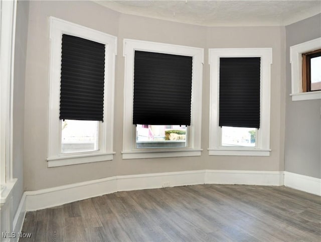 unfurnished room with a textured ceiling, baseboards, and wood finished floors