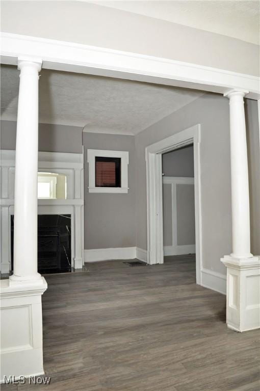 unfurnished living room with ornate columns, baseboards, and dark wood-style floors