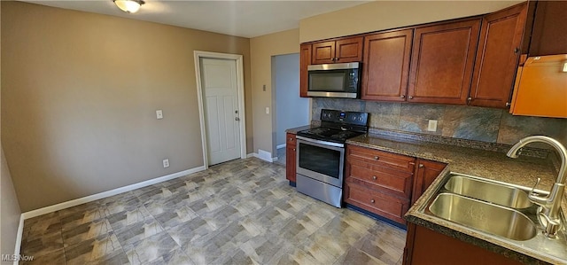 kitchen featuring a sink, baseboards, appliances with stainless steel finishes, backsplash, and dark countertops