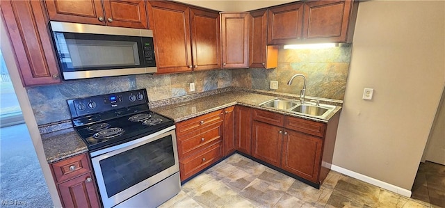 kitchen featuring baseboards, decorative backsplash, dark stone countertops, stainless steel appliances, and a sink