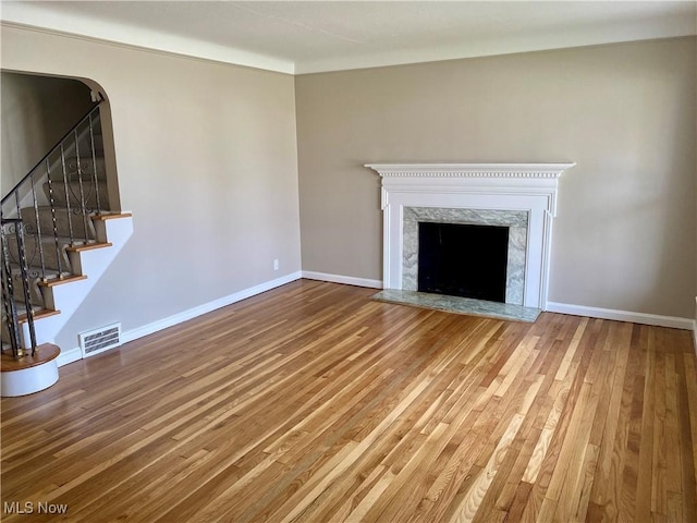 unfurnished living room with baseboards, visible vents, hardwood / wood-style floors, and a high end fireplace