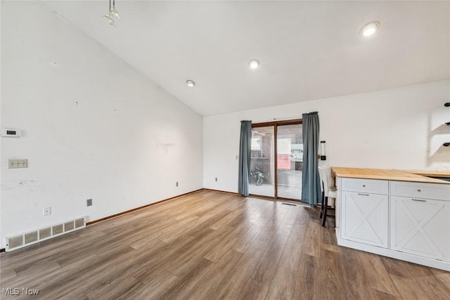 unfurnished living room with baseboards, visible vents, lofted ceiling, wood finished floors, and recessed lighting