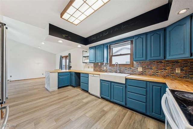 kitchen featuring a peninsula, white appliances, a sink, blue cabinetry, and backsplash