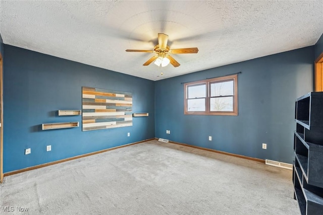 carpeted empty room with visible vents, a textured ceiling, baseboards, and a ceiling fan