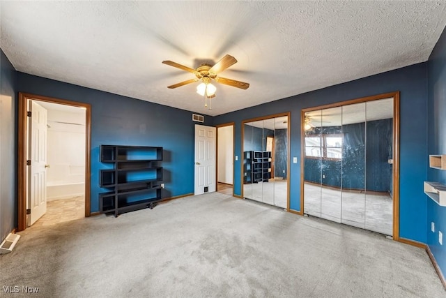 unfurnished bedroom featuring carpet, a textured ceiling, ceiling fan, and two closets