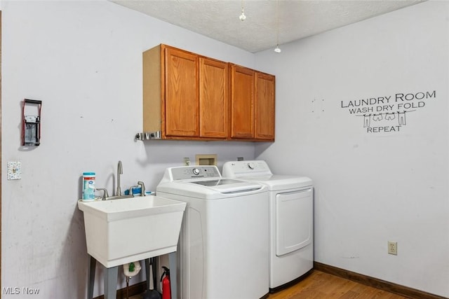 laundry room with cabinet space, baseboards, light wood-style flooring, independent washer and dryer, and a textured ceiling