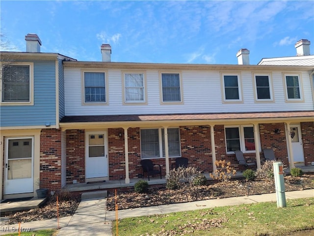 townhome / multi-family property featuring covered porch, a chimney, and brick siding