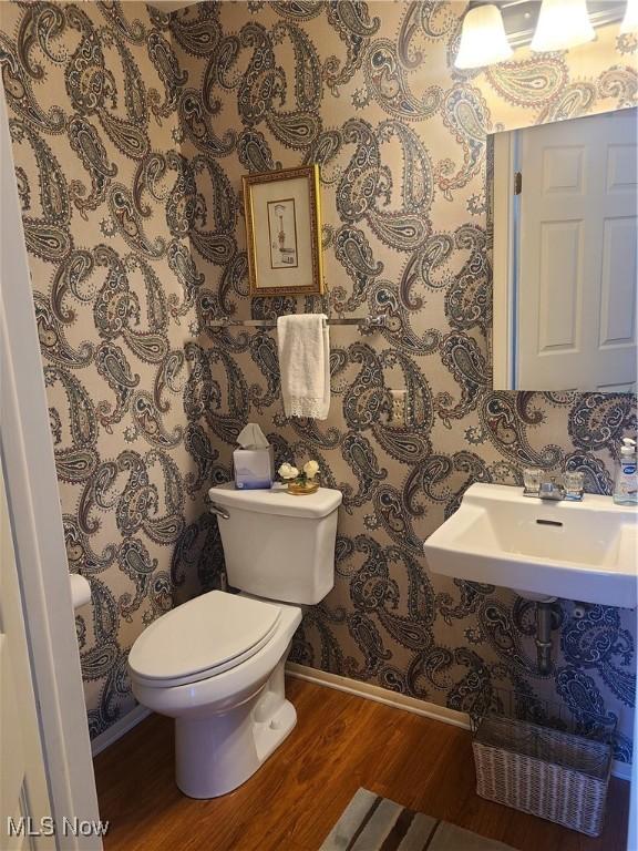 bathroom with toilet, a sink, wood finished floors, baseboards, and wallpapered walls