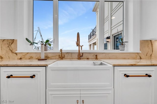 kitchen with tasteful backsplash, white cabinetry, light stone counters, and a sink