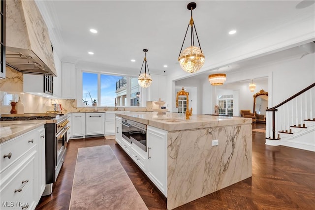 kitchen featuring custom exhaust hood, stainless steel stove, a spacious island, light stone countertops, and backsplash