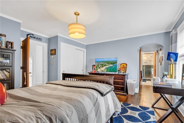 bedroom featuring ornamental molding, arched walkways, wood finished floors, and a closet