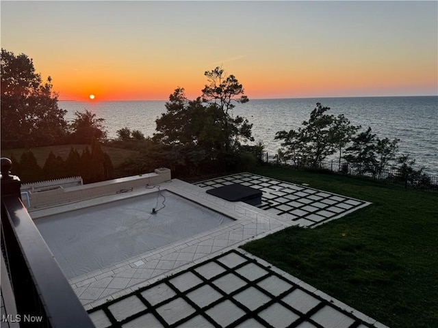 patio terrace at dusk featuring a water view and a yard