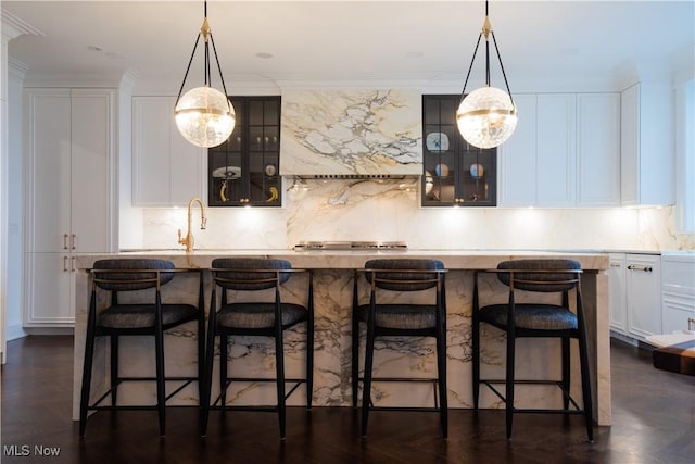 kitchen with backsplash, white cabinetry, a kitchen island with sink, and ventilation hood