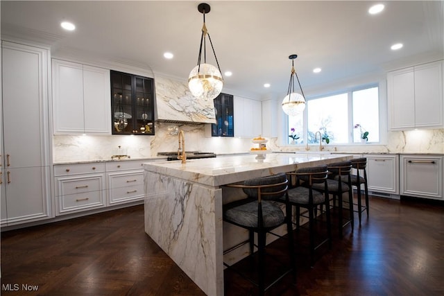 kitchen featuring a breakfast bar, light stone counters, glass insert cabinets, a center island with sink, and decorative backsplash