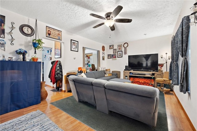 living room with ceiling fan, a textured ceiling, and light wood finished floors