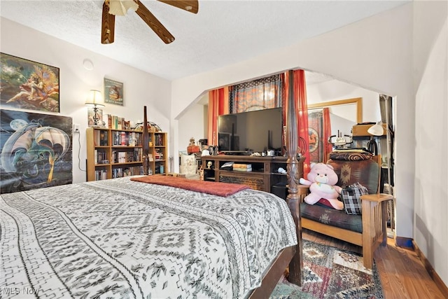 bedroom featuring ceiling fan, a textured ceiling, baseboards, and wood finished floors