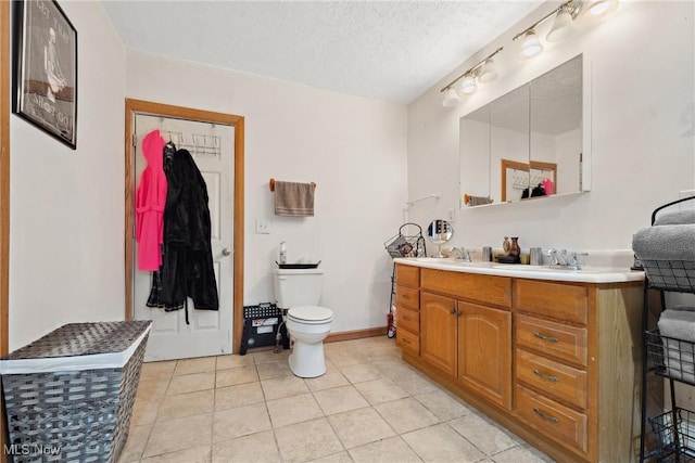 bathroom featuring double vanity, toilet, a sink, a textured ceiling, and tile patterned floors