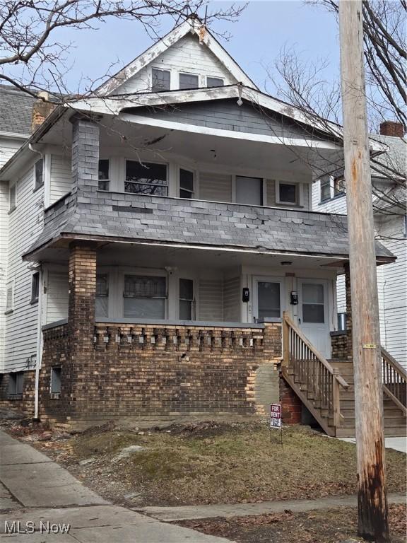 view of front of house featuring a porch, brick siding, a balcony, and stairs