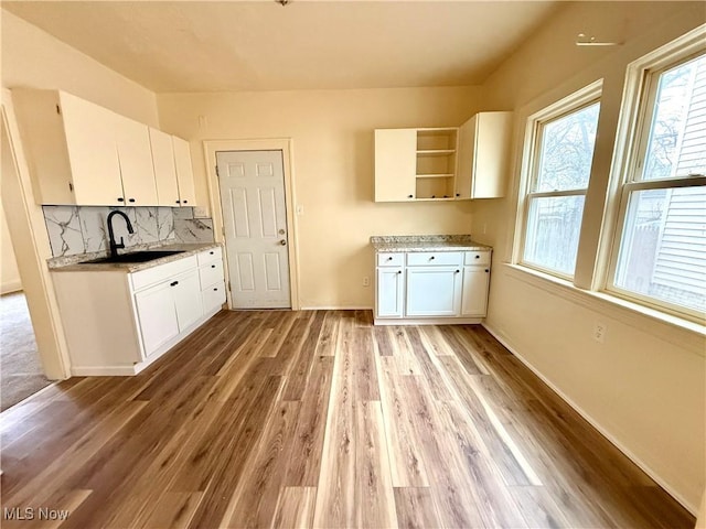 kitchen with light wood-type flooring, white cabinetry, open shelves, and a sink