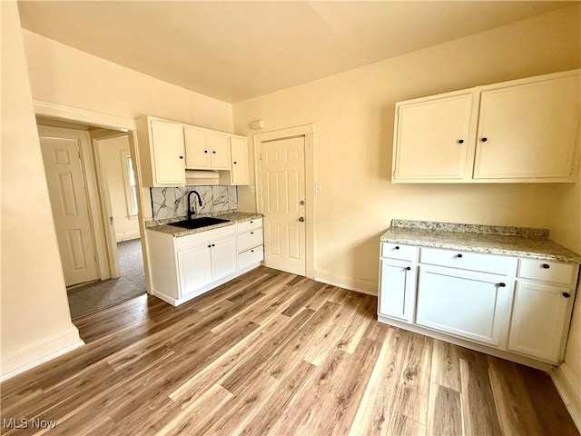 kitchen featuring a sink, white cabinetry, baseboards, light wood-type flooring, and decorative backsplash