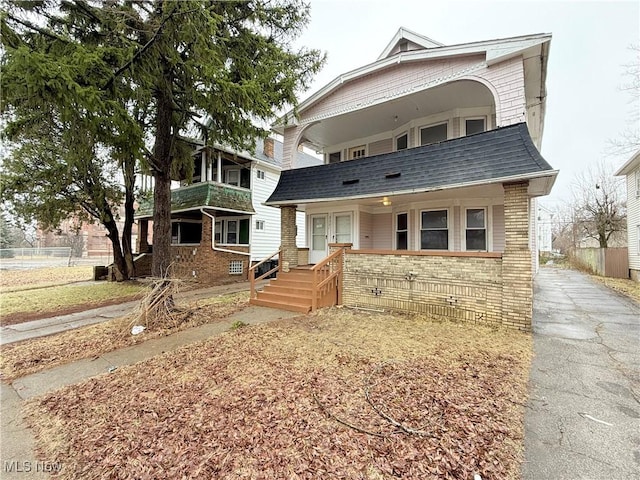 view of front facade with a porch, brick siding, and a shingled roof