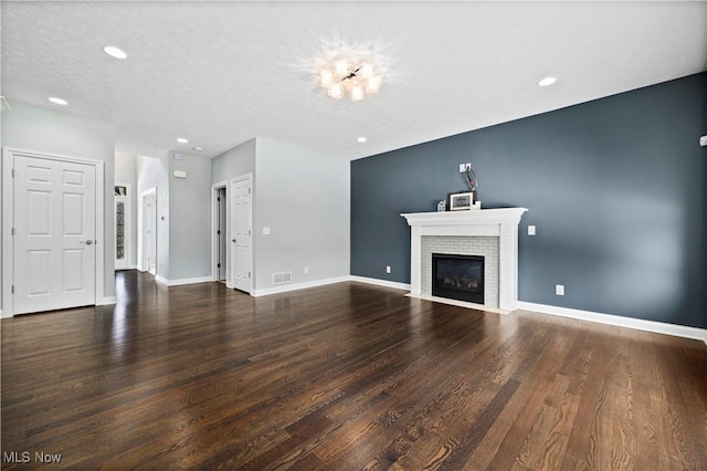 unfurnished living room featuring a textured ceiling, a fireplace with flush hearth, wood finished floors, visible vents, and baseboards