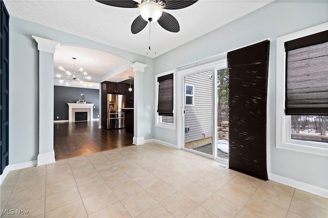 empty room featuring light tile patterned floors, ceiling fan with notable chandelier, decorative columns, and baseboards