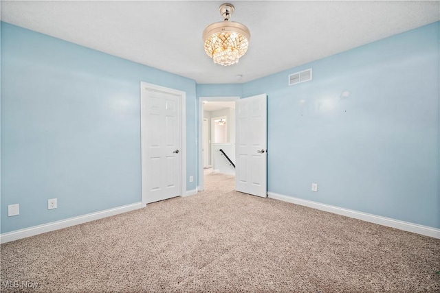 carpeted empty room featuring a chandelier, visible vents, and baseboards