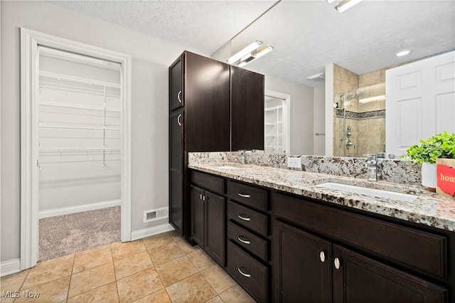 bathroom with a textured ceiling, a sink, a walk in closet, and a shower stall