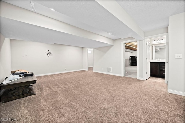 finished below grade area featuring a textured ceiling, a sink, visible vents, baseboards, and carpet