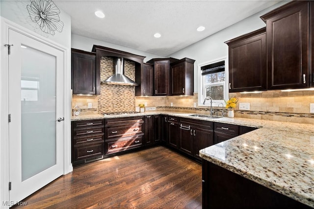 kitchen featuring dark wood-style floors, wall chimney exhaust hood, light stone countertops, stainless steel gas cooktop, and a sink