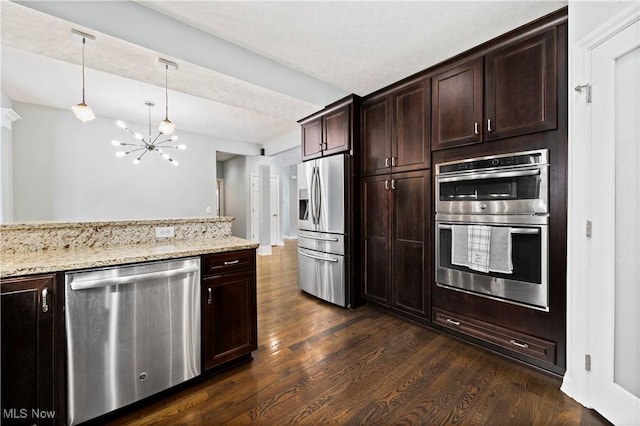 kitchen featuring dark brown cabinetry, appliances with stainless steel finishes, dark wood-style flooring, decorative light fixtures, and light stone countertops